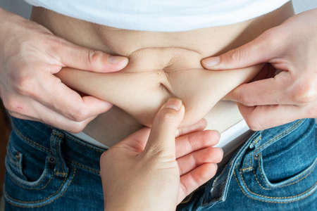 Cropped shot of someone touching and pulling another one cellulite fat belly. Conceptual of unhealthy body and fatty.の写真素材