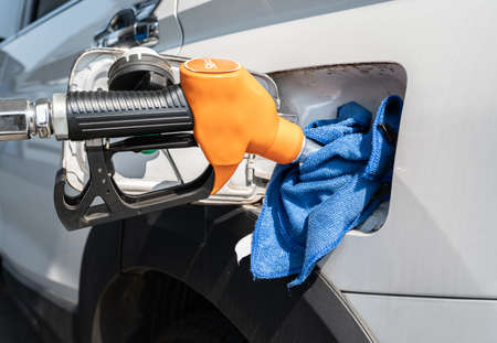 An orange nozzle while refueling gasoline to fuel tank of car in gas station. Gas station is a...