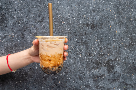 Cropped shot of someone hand holding a cup of iced Bubble milk tea with big straw. Bubble tea was a traditional drink in Taiwan before it became hugely popular all over the world.の写真素材