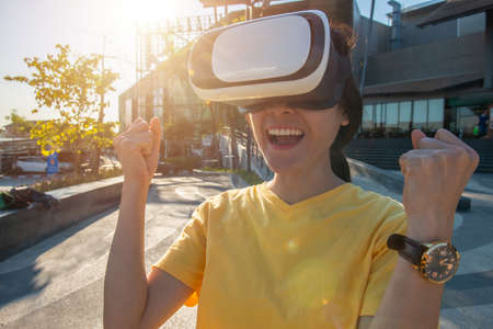 Portrait of young Asian woman wearing virtual reality goggles and enjoying the VR simulation...