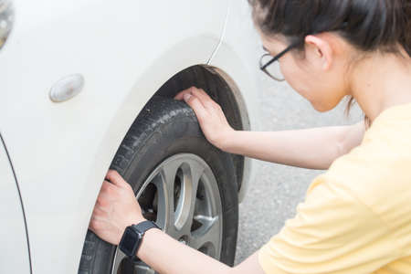 Cropped shot of young woman touching and checking her car tyre. She worrying about somethings wrong...
