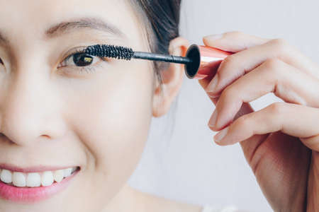 Close-up of young Asian woman applying black mascara on her eyelashes with makeup brush. Mascara is a cosmetic commonly used to enhance the eyelashes.の写真素材