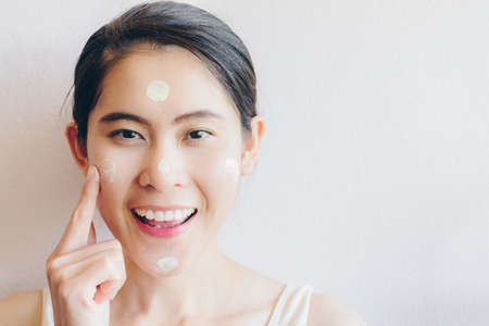 Portrait of Asian woman marking and applying cream concealer on her facial skin. Concealer is a type of cosmetic that is used to mask dark circles, age spots, large pores etc.の写真素材