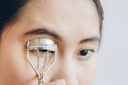 Closeup of young Asian woman using eyelash curler. Eyelash curler is a hand-operated mechanical device for curling eyelashes for cosmetic purposes.の写真素材
