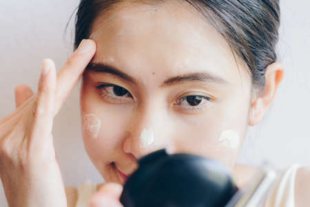 Close up shot of Asian woman trying to marking and applying cream concealer on her facial skin. Concealer is a type of cosmetic that is used to mask dark circles, age spots, large pores etc.の写真素材