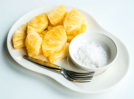 Closeup of a sliced pieces of fresh pineapple served with salt with isolated white table. Adding salt to pineapple suppresses the bitter flavor of the fruit.の写真素材
