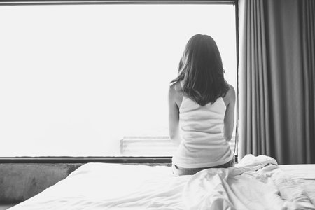 Portrait of depressed woman sitting alone on bed in bedroom. Conceptual of broken hearted, sadness, loneliness woman. Shot with black and white tone.の写真素材