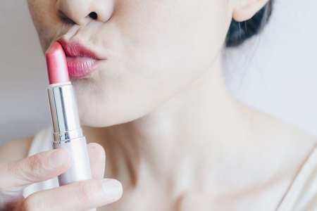 Cropped shot of woman holding and kiss a lipstick and applying on her lips. Conceptual of beauty and cosmetics shot.の写真素材