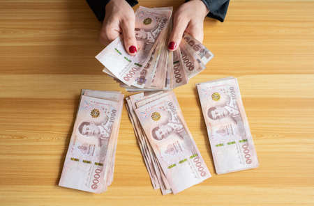 An accountant woman sitting and  counting a piles of Thai baht banknotes. The baht is the official currency of Thailand.の写真素材