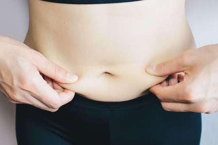 Cropped shot of Woman touching her cellulite fat belly, woman's hand holding excessive belly fat.
