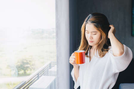 Portrait of young Asian woman drinking coffee near the window in bedroom after her wake up in the morning.の写真素材