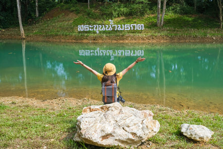 Back view of happiness woman tourist sitting on the rock with the beautiful green lagoon of Khun Nam Nang Non forest park in Chiang Rai province of Thailand.の写真素材