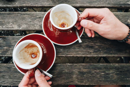 Close up of human hands touching empty couple cup of coffee on the wooden table. Remains of coffee stain after drink.の写真素材