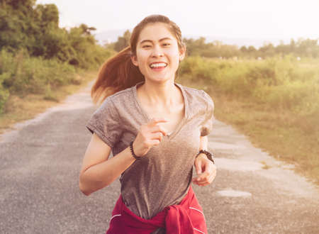 Young fitness woman running on the countryside road in the evening. Conceptual shot of Healthy and lifestyle of woman while doing workout.の写真素材