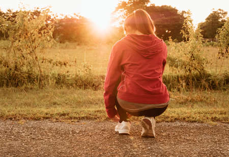 Woman tying running shoes getting ready for trails running in the evening. Sport and recreation concept.の写真素材
