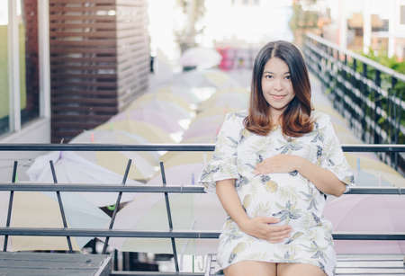 Portrait of young Asian pregnant woman sitting and touching her belly with her hands. Conceptual of...