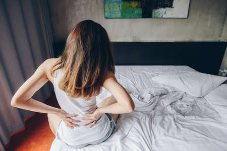 Back view of young woman suffering from Backache or Sore waist after her wake up in the bedroom. Conceptual of woman stretching suffering from sudden back pain.の写真素材
