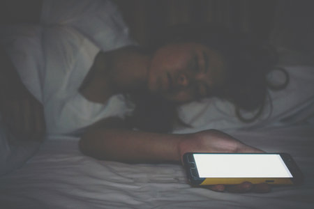 Woman sleeping on bed with her cell phone on night stand. Every person surrounded by technology even...