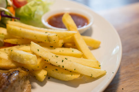 Close-up of French fries serving with salad on the wooden table.