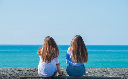 <p>Two teenager sister relax by sitting at the black sand beach of Napier town. Summer holiday in New Zealand.</p>の写真素材