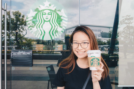 Chiang Rai, Thailand : May-23-2018 : Happy Asian girl showing a cup of Starbucks coffee in front of Starbucks coffee store.のeditorial素材