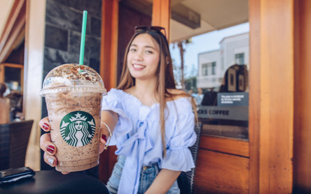 Napier, New Zealand -April/01/2018- : Asian women holding and showing her cup of Starbucks Frappuccino in Napier Starbucks coffee shop.のeditorial素材