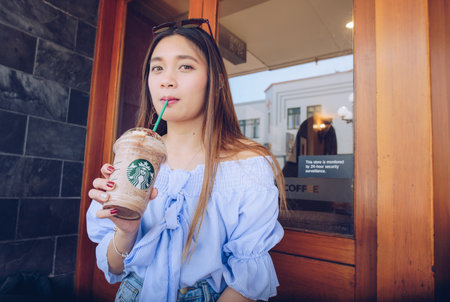 Napier, New Zealand -April/01/2018- : Asian women drinking and holding a cup of Starbucks Frappuccino in Napier Starbucks coffee shop.のeditorial素材