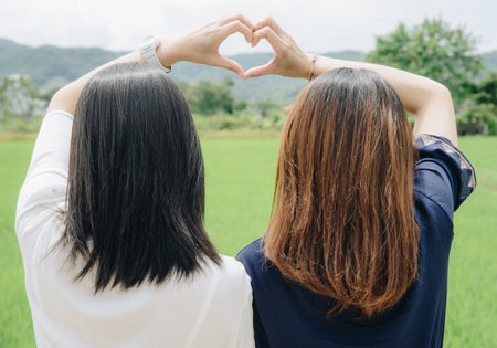 Cropped shot view of two women showing hands like the heart shape. Back view.の写真素材