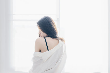 Asian woman standing near the window after her wake up in the morning, back view.の写真素材