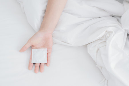 Cropped shot view of woman hand with condom on the bed.の写真素材