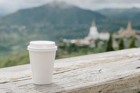 A paper cup of coffee on the wooden table with a spectacular view.の写真素材