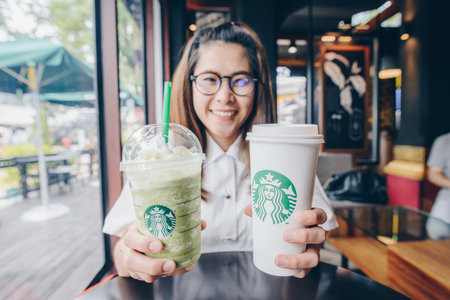 CHIANG MAI, THAILAND- July-24-2017 : Asian girl holding a cup of Venti size Starbucks coffee and Green tea latte frappuccino in Starbucks coffee shop.のeditorial素材