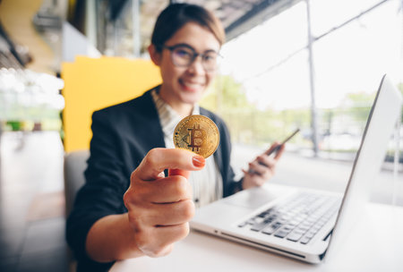 Happiness businesswoman holding a golden Bitcoin token (focus at bitcoin). Bitcoin is one of the popular cryptocurrency, a virtual currency or a digital currency.の写真素材
