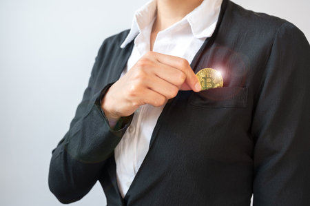 Businesswoman collecting a golden Bitcoin token in her suit pocket. Bitcoin is one of the popular cryptocurrency, a virtual currency or a digital currency.の写真素材