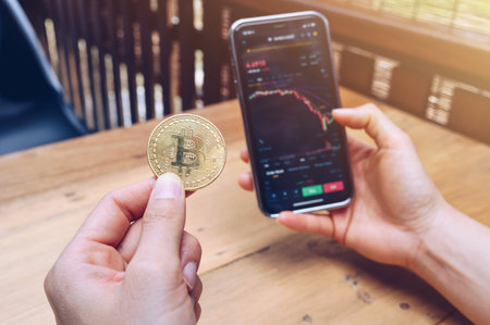 Someone checking Bitcoin price chart on digital exchange on smartphone while holding Bitcoin token....