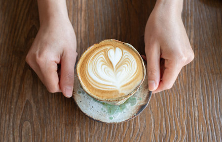 Someone hands holding a cup of hot Cappuccino coffee before drinking. The taste of cappuccinos can be described as creamy, smooth, and balanced.の写真素材