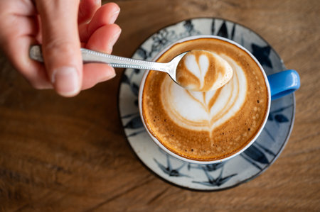 Someone scooping creamy surface of hot latte coffee. A latte is a coffee drink made with espresso...