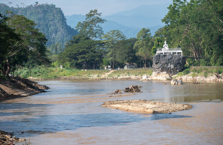 A white Buddha statue situated on the rock nearly Mae Kok river in Chiang Rai province, Thailand. The river originates in the Shan State of Burma.の写真素材