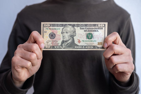 Cropped shot view of woman holding and showing ten American dollar banknotes in hands. The US Dollar...