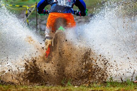 enduro rides through the mud with big splash,driver splashing mud on wet and muddy terrain,Motocross racer in a wet and muddy terrain covering the driver completely.の写真素材