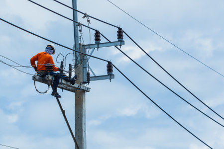 Electrician working on high voltage power pole with blue sky background.の写真素材