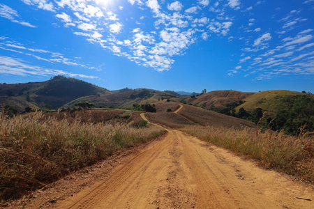 Dirt road in the mountains and blue sky with white clouds.