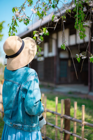 Woman in a hat and blue dress standing in front of a Japanese houseの写真素材
