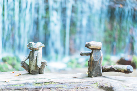 Miniature man and woman sitting on a log in front of waterfall at Karuizawaの写真素材