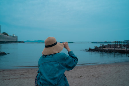 A woman in a hat looks at the sea in the evening.