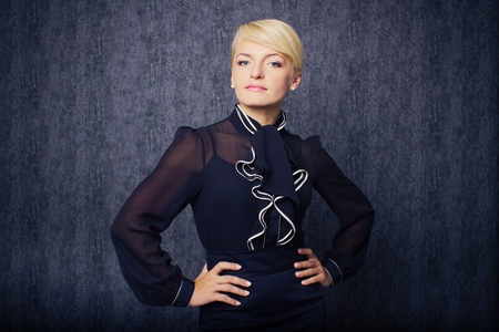 Blonde business woman in black suit staying in front of dark wallの写真素材