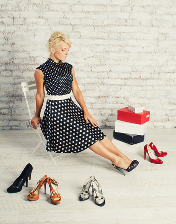 Young blonde girl in dress sitting in a chair and choosing shoes in the shopの写真素材