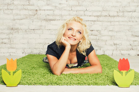 Carefree smiling young blonde women in dress lying on the grass with flowers in studioの写真素材