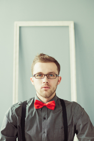 Young man in red bowtie and suspenders looking straight at cameraの写真素材