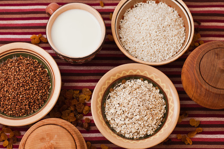 Photo of buckwheat, oat flakes, rice and milk in platesの写真素材